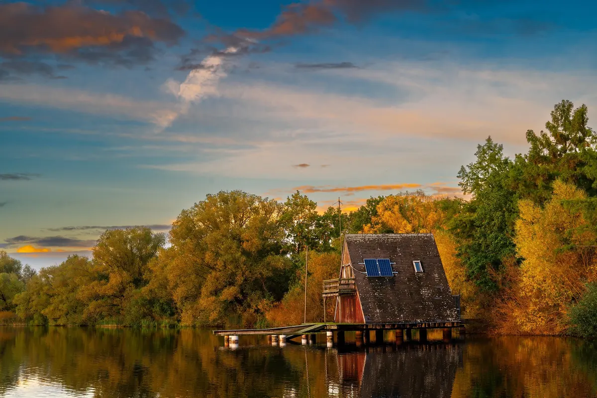 A-Frame-Ferienhaus auf Stelzen am stillen See im herbstlichen Wald bei Abendlicht
