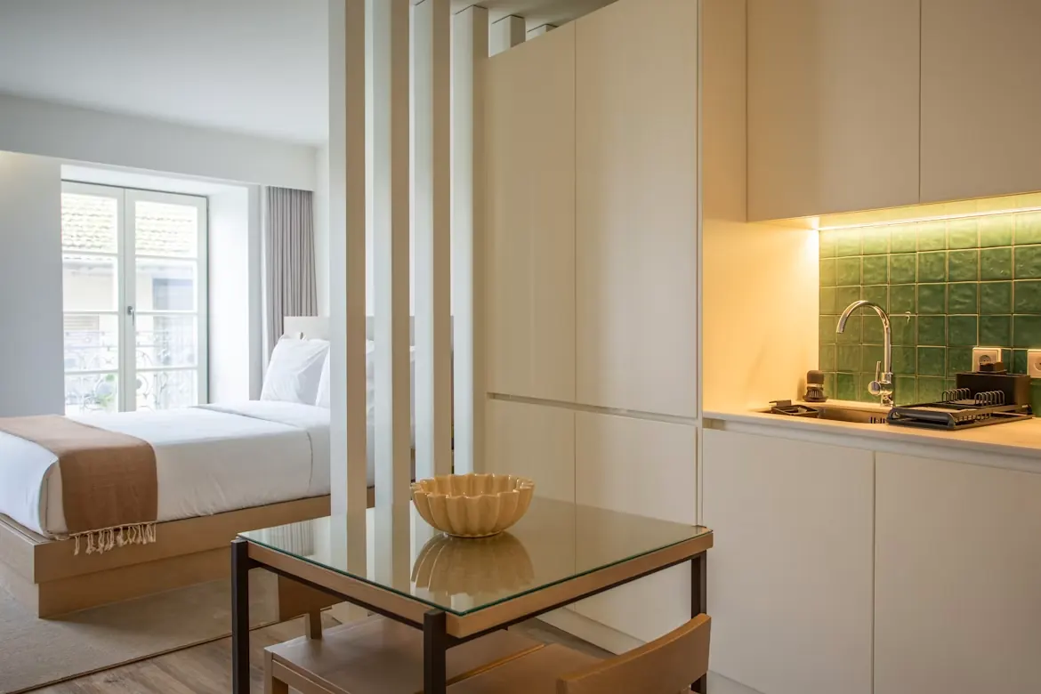 Moderne helle Ferienwohnung mit Holzlatten-Trennwand, Bett in Weiß und offener Küche mit grüner Fliese