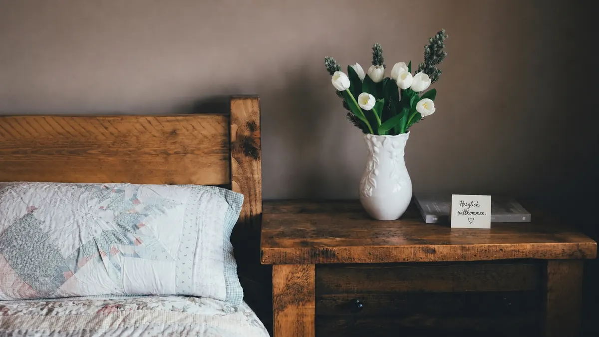 Nachttisch mit Wildblumen, Tee und einer handgeschriebenen Karte „Herzlich Willkommen“ – ein stiller Willkommensmoment.